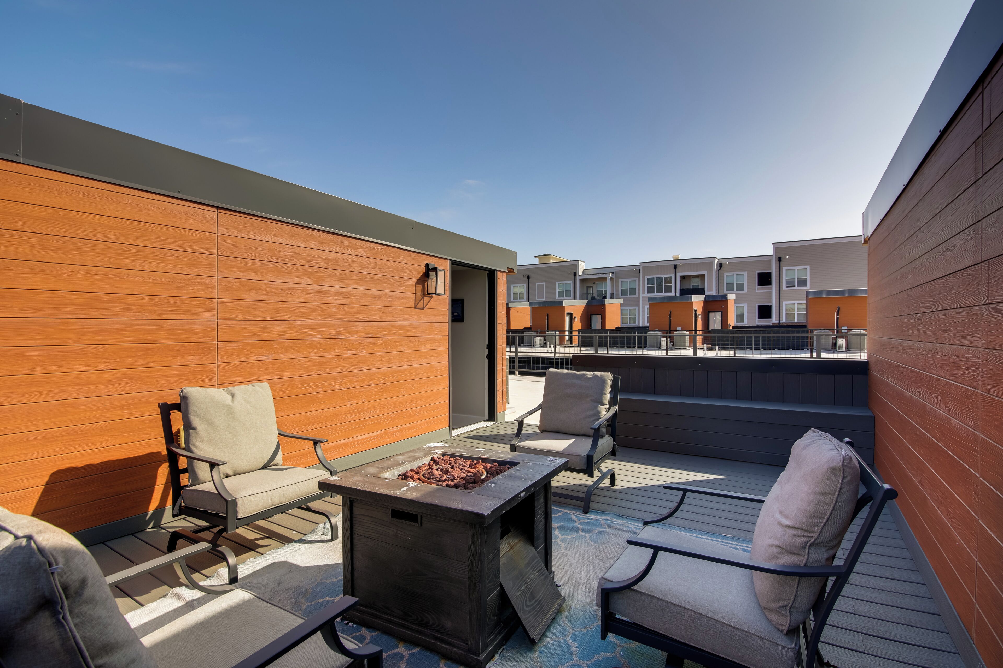 A rooftop patio with outdoor seating, a fire pit, and a view of adjacent buildings.