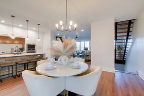 A modern kitchen with white cabinets, a central island with stools, and a dining area with a round table and chairs. - Walk to Fedex Forum! Luxe Townhome w/ Rooftop Deck (Memphis)
