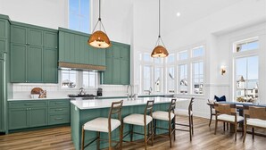 A modern kitchen with green cabinets, a large island with bar stools, and pendant lighting. - Pet-Friendly Coastal Hub w/ Gulf Views, Dual Living Areas & Family Layout (Port Aransas)