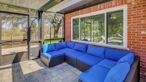 A covered patio area with a sectional sofa, a glass door leading outside, and a brick wall with large windows. - 3 Mi to Water! Pet-friendly Retreat in Lake Wales (Lake Wales)