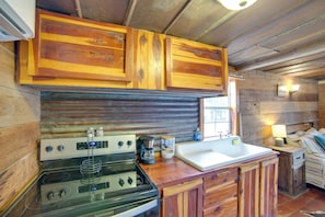 A rustic kitchen with wooden cabinets, a stove, a coffee maker, and a sink. - Couples Getaway w/ Ranch Views - Near Lavon Lake! (Blue Ridge)