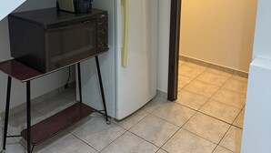 Een compacte keuken met een koelkast, koffiezetapparaat en een klein tafeltje met een bankje.