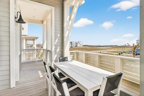 A covered outdoor patio with a white table and chairs, a pergola, and a view of buildings and a road. - Red White and Saguaro 246 DEW (Port Aransas)