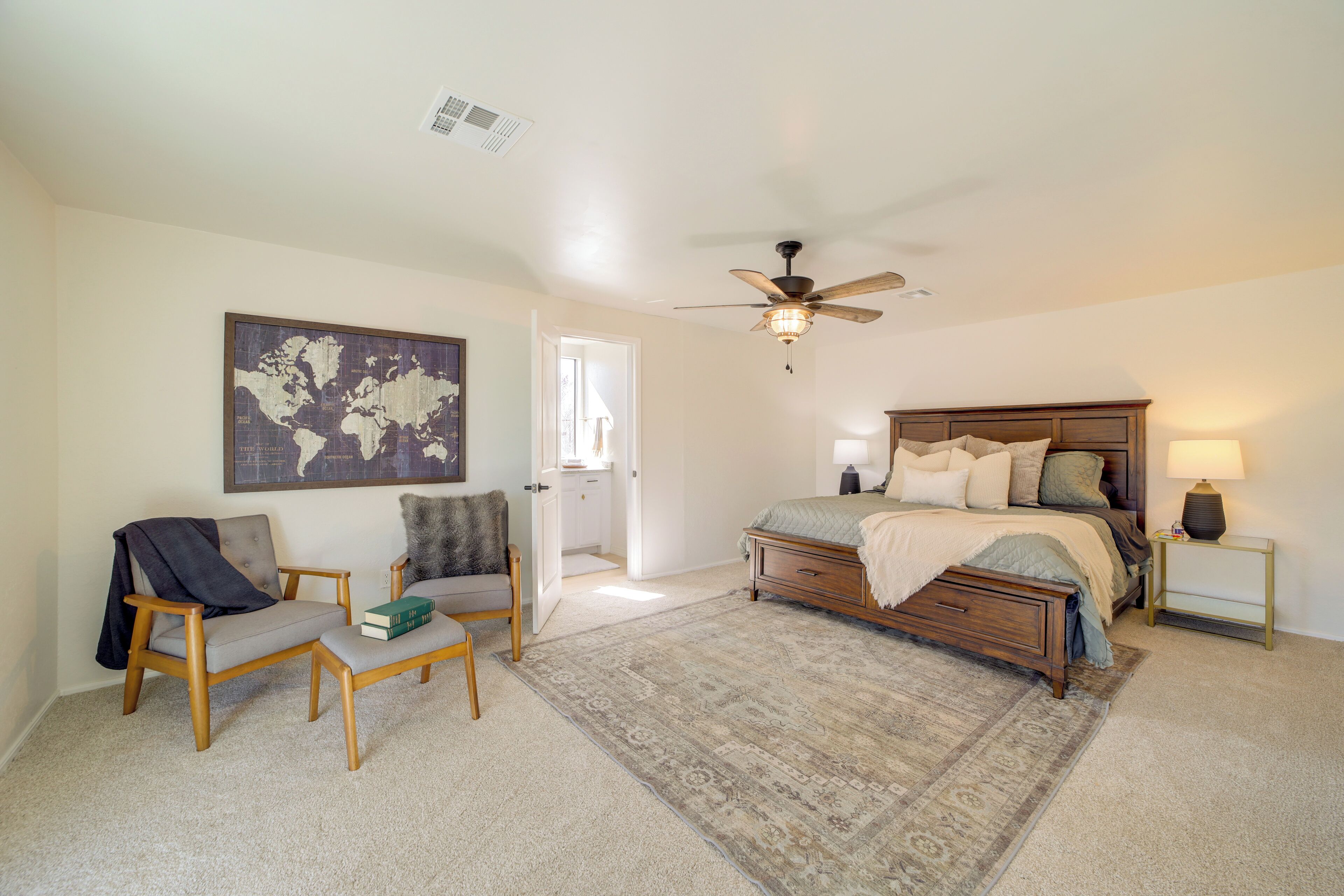 A bedroom with a bed, a chair, a desk, a world map on the wall, and a ceiling fan.