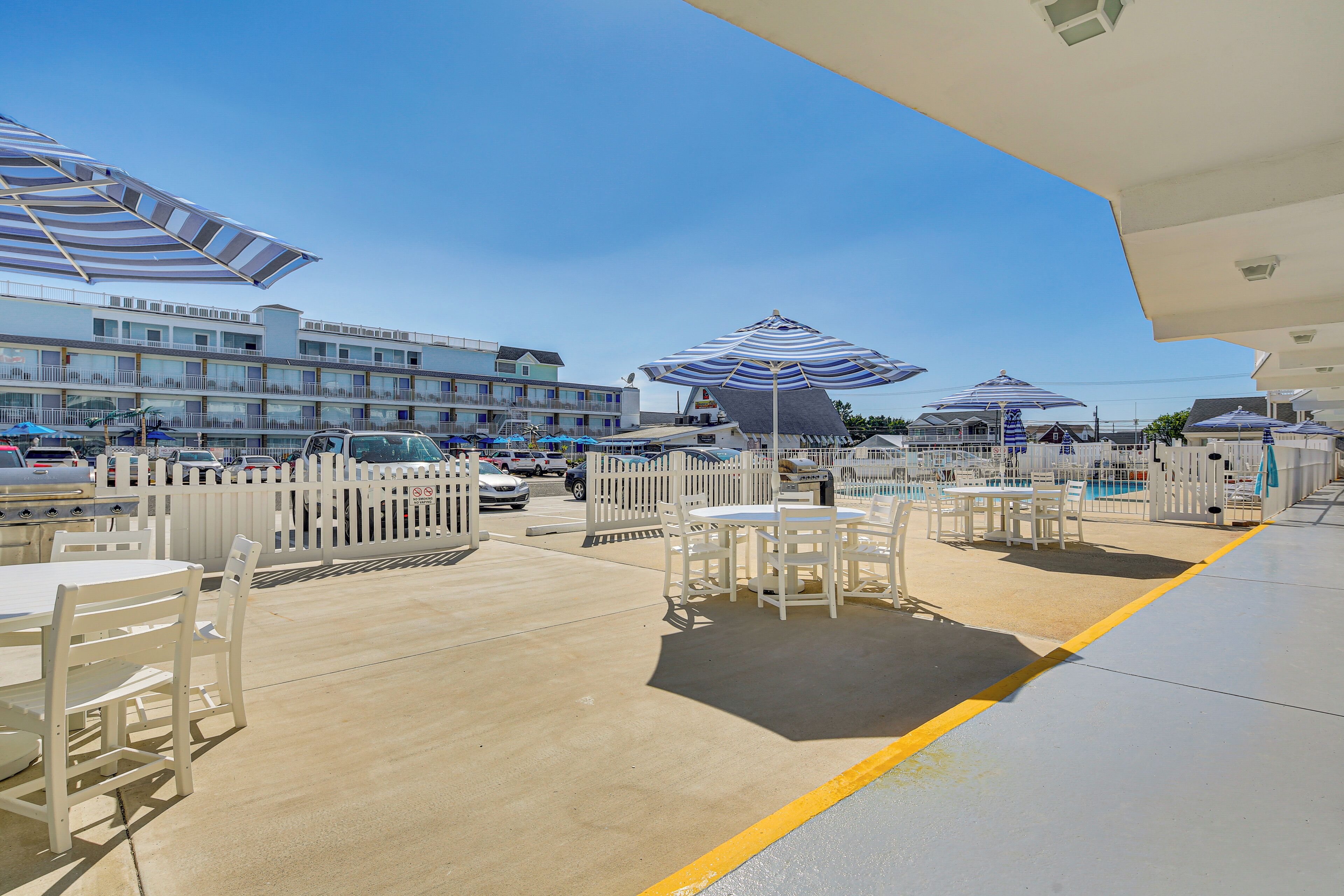 An outdoor seating area with tables and chairs, umbrellas, and a pool in the background.