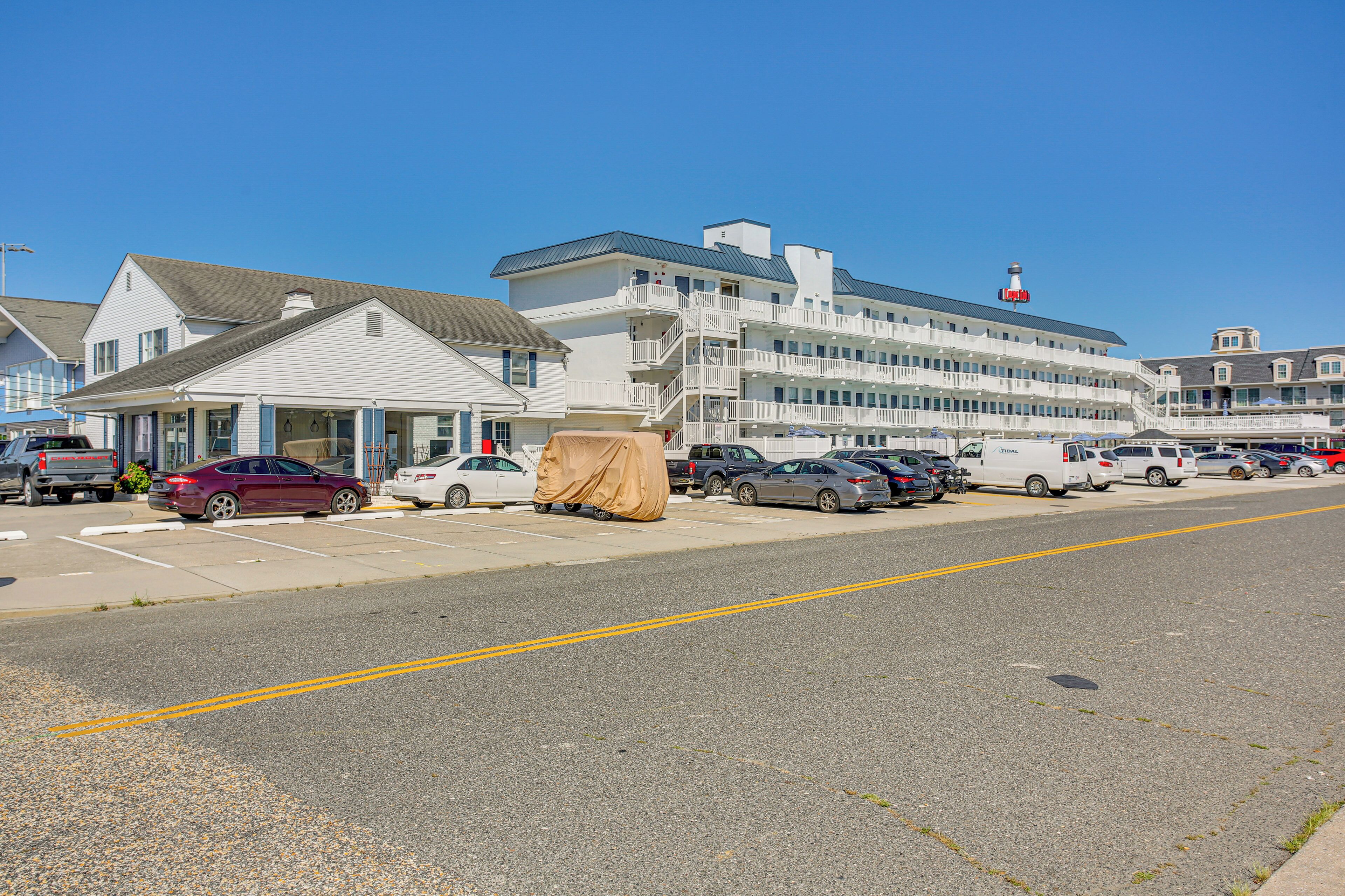 A multi-story hotel with a prominent lighthouse on top, parking spaces, and a covered area.