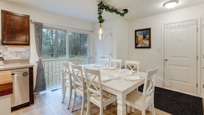 A dining area with a white table and chairs, a wooden cabinet, and a window with a view of trees. - Deck & EV Charger: Coastal Retreat 1 Mi to Marina (Greenbackville)
