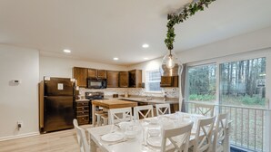 A modern kitchen with wooden cabinets, a stainless steel refrigerator, and a dining area with a white table set for six. - Deck & EV Charger: Coastal Retreat 1 Mi to Marina (Greenbackville)