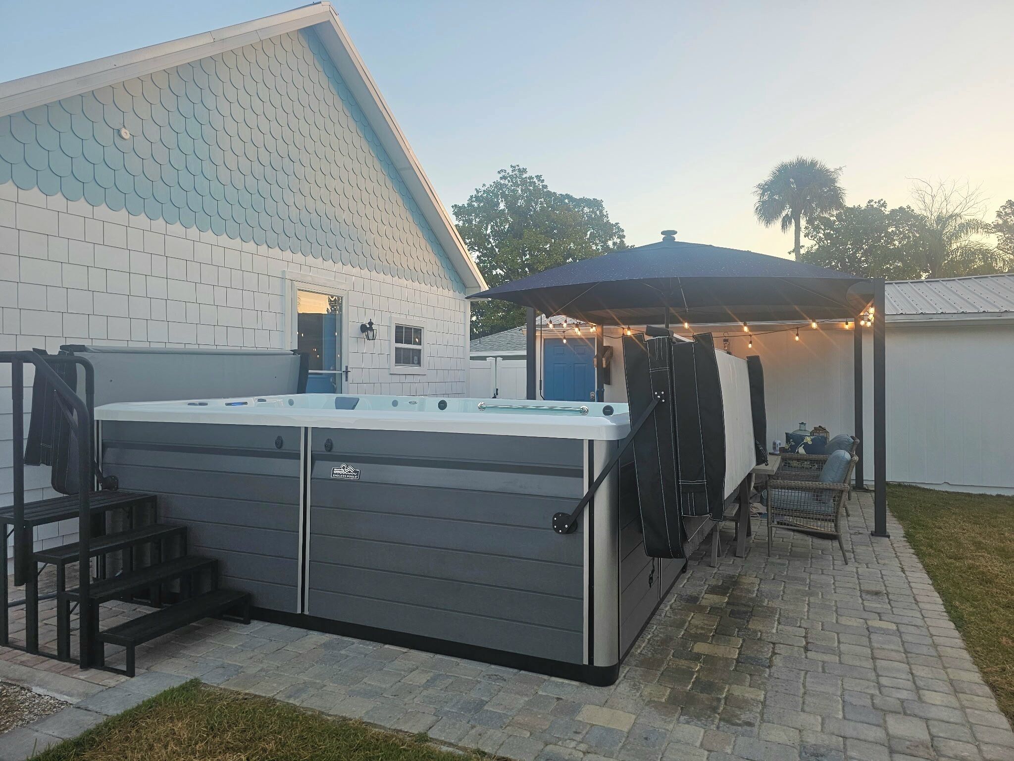 A hot tub in a backyard with a covered patio area and string lights.