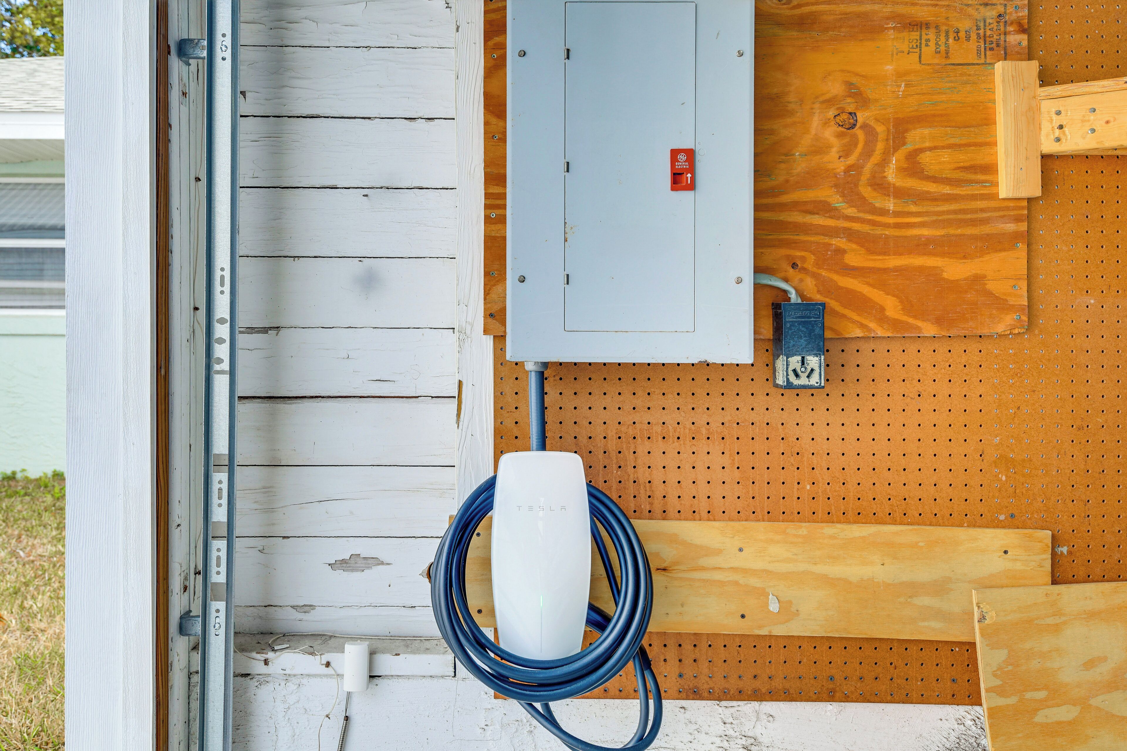 Een Tesla laadstation bevestigd aan een houten wand, met een metalen stroomkast en een gatenbord.