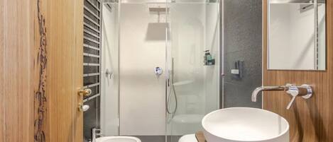 A modern bathroom with a glass-enclosed shower, a white sink, and a wooden vanity.