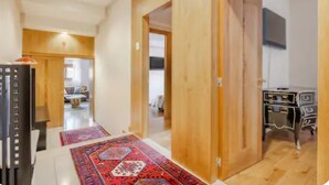 Een gang met houten deuren, een bureau en een aan de muur bevestigde televisie.