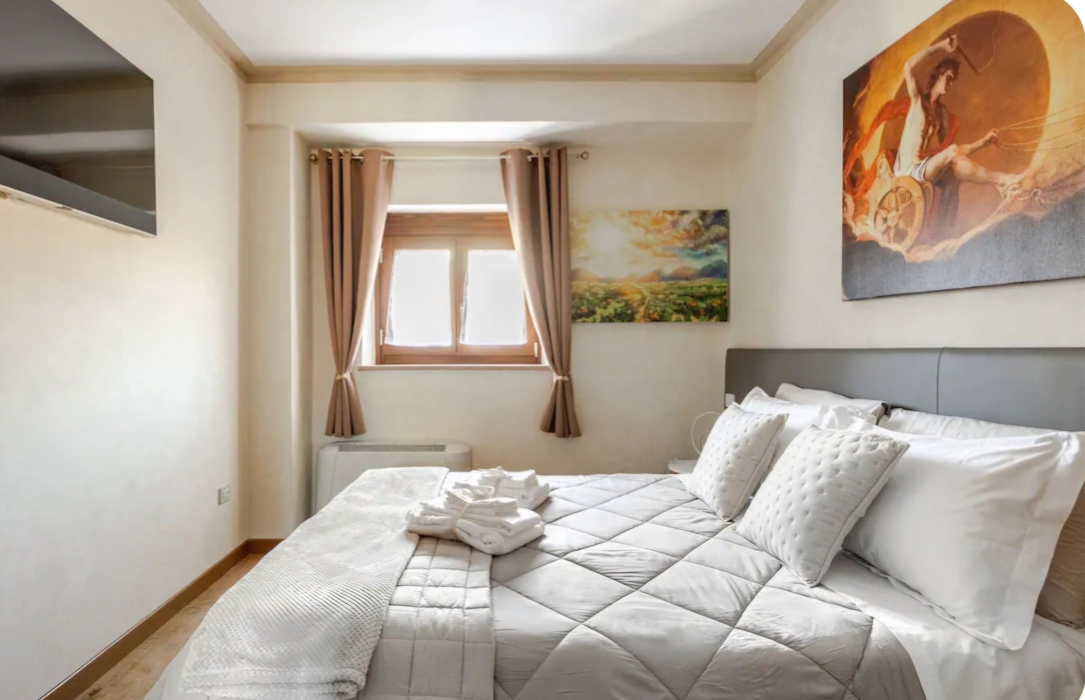 A neatly made bed with a quilt, a window with curtains, and a painting on the wall.