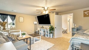 Un salon bien éclairé, doté d’un ventilateur de plafond, d’un téléviseur à écran plat, d’un canapé, d’une table basse et d’un lit avec une literie à motifs.