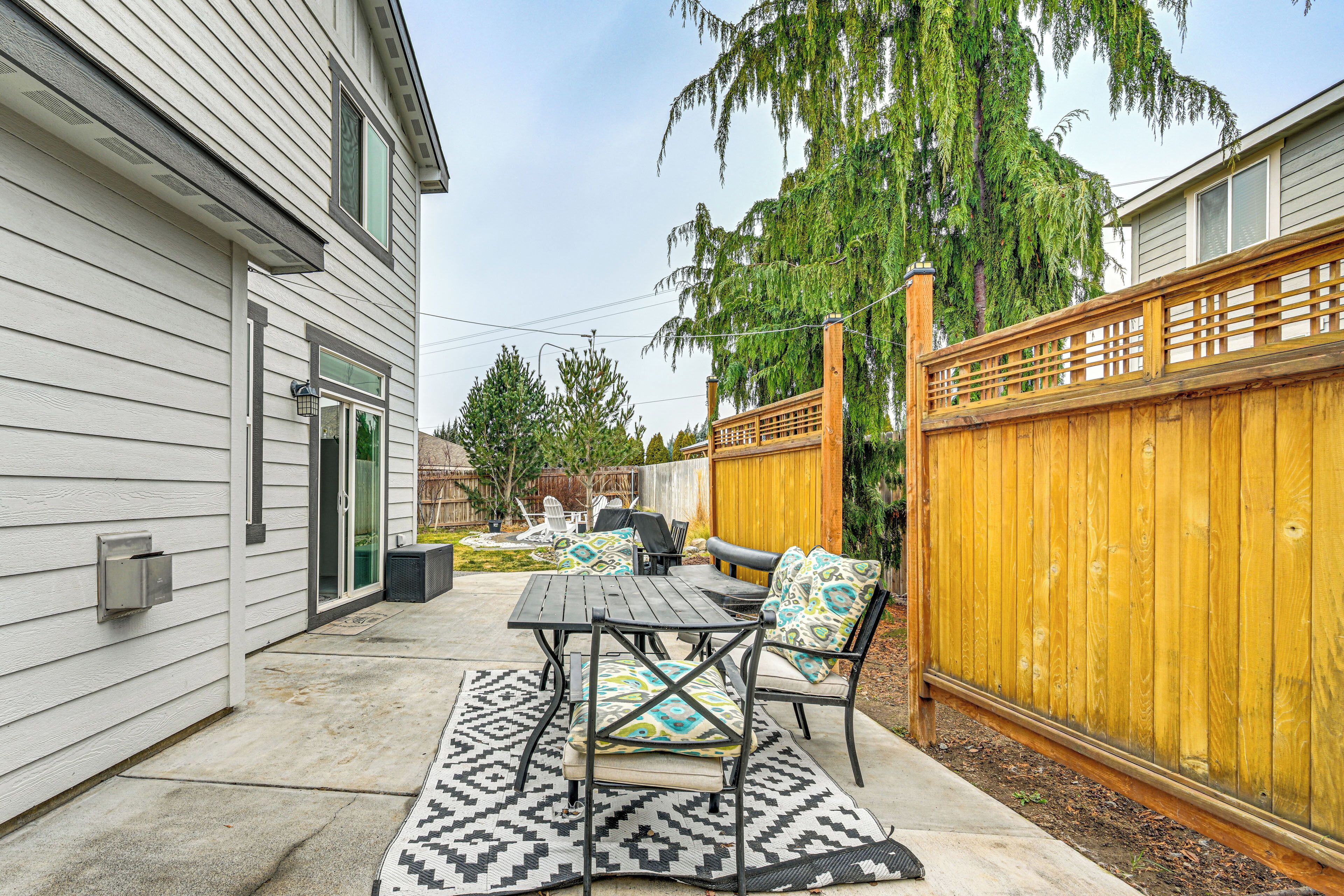 A patio with a table and chairs, a patterned rug, and a wooden fence.