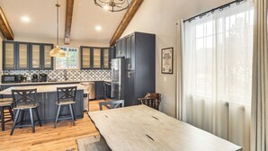 Eine moderne Küche mit dunklen Schränken, einer zentralen Kochinsel mit Barhocker, einem großen Holztisch und einer Pendelleuchte.