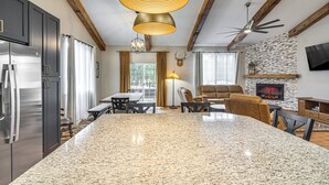 Eine moderne Küche mit Granit-Arbeitsplatten, Edelstahlgeräten und einer großen Kochinsel. Es gibt einen Essbereich mit Tisch und Stühlen, und ein Kamin im Wohnzimmer.