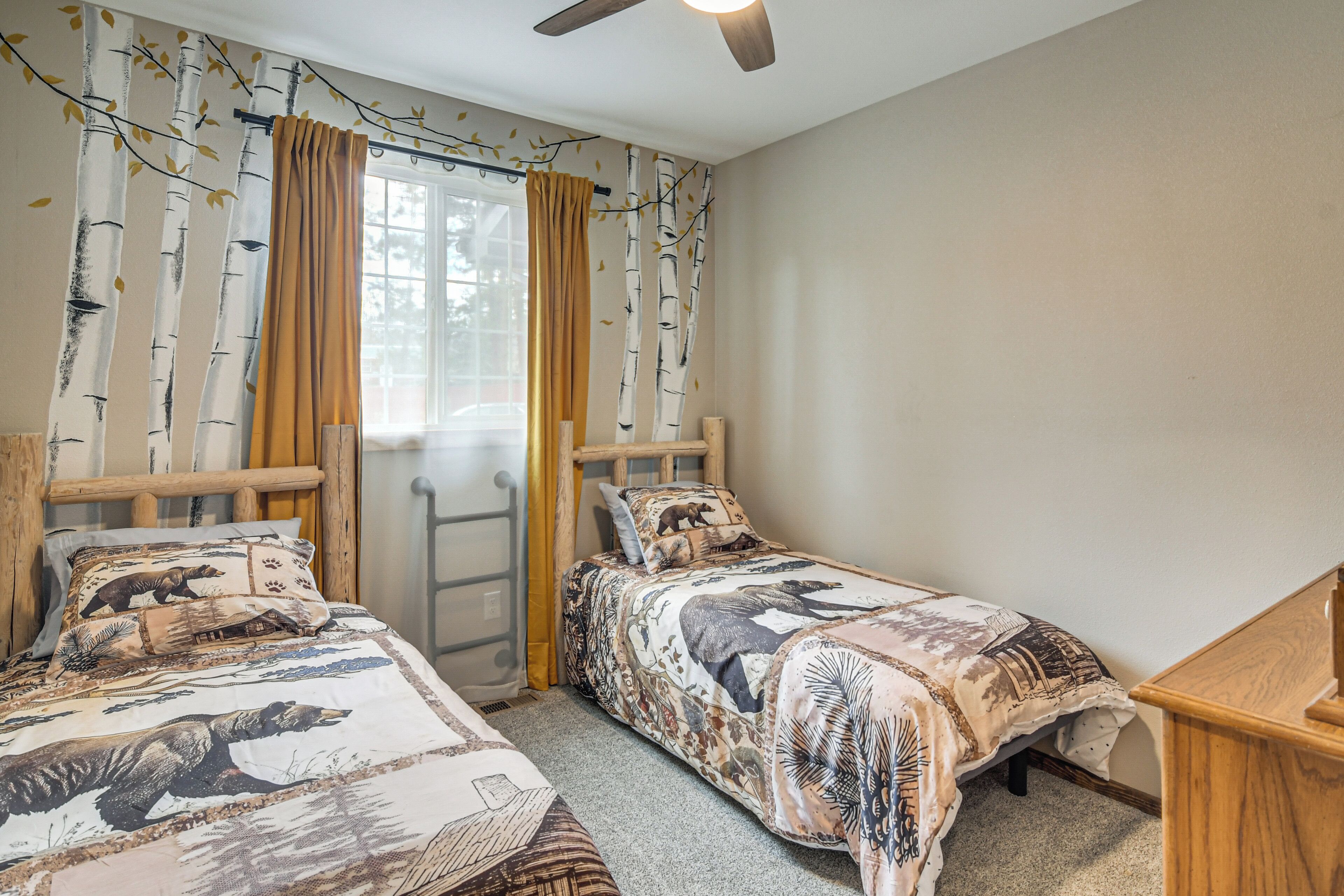 A bedroom with two single beds, a wooden headboard, a window with curtains, and a ceiling fan.