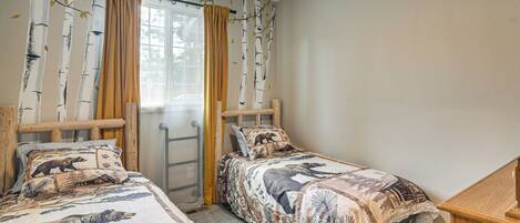 A bedroom with two single beds, a wooden headboard, a window with curtains, and a ceiling fan.
