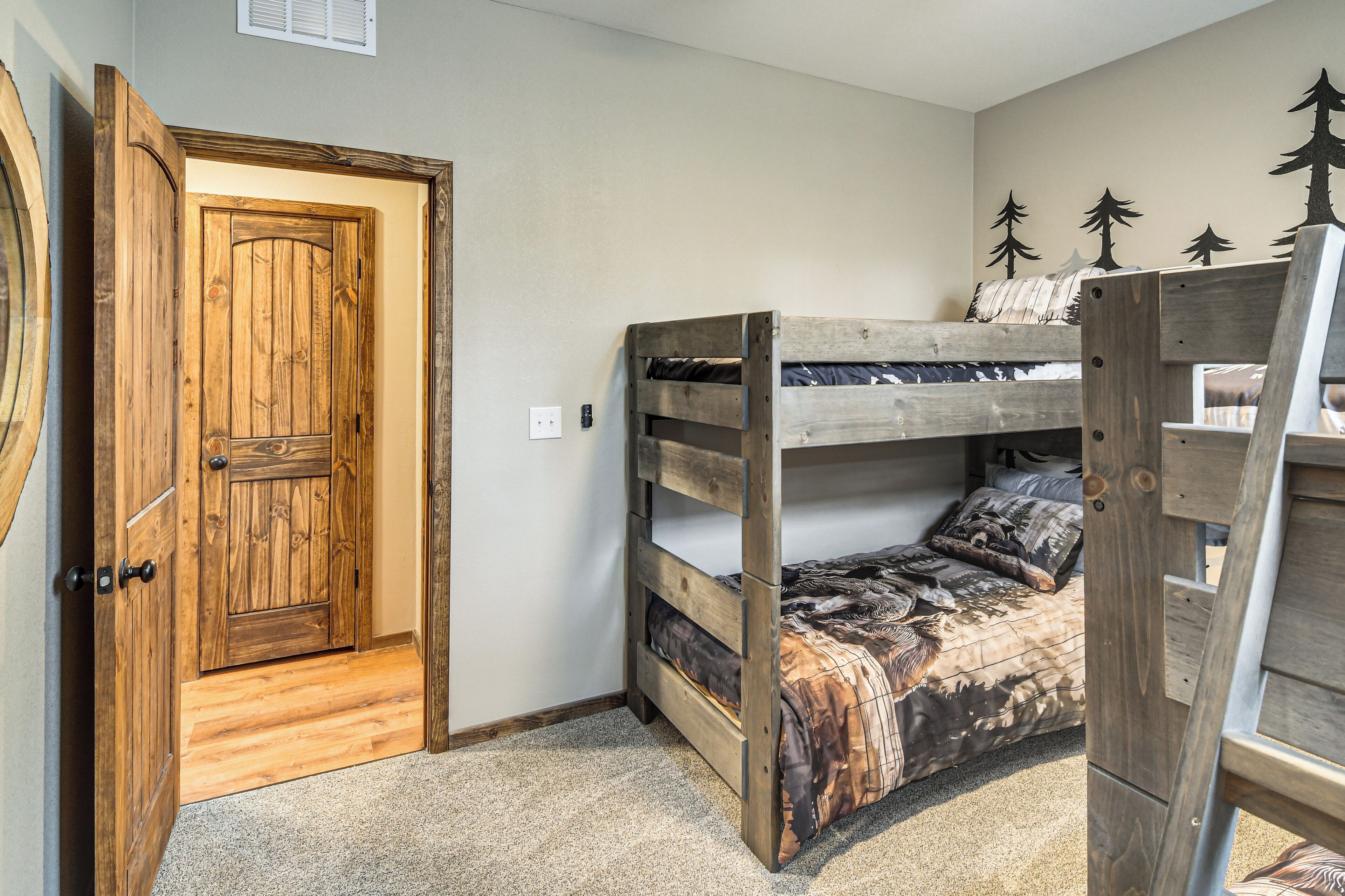 Una cama litera con edredón estampado con un diseño de camuflaje, una puerta de madera y un adhesivo mural con motivos de árboles.