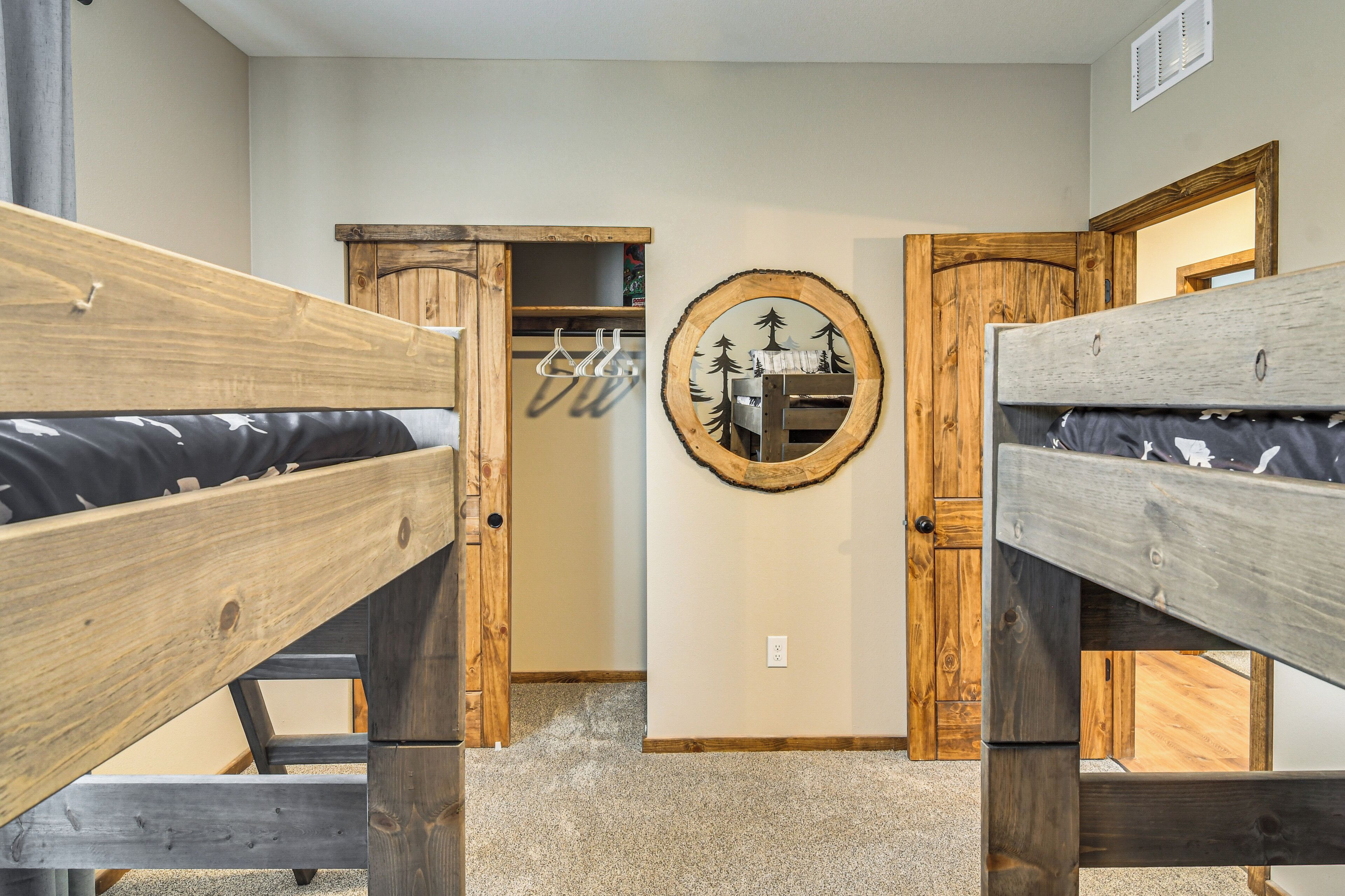Une chambre avec des lits superposés, une armoire en bois et un miroir orné d’un motif d’arbre.