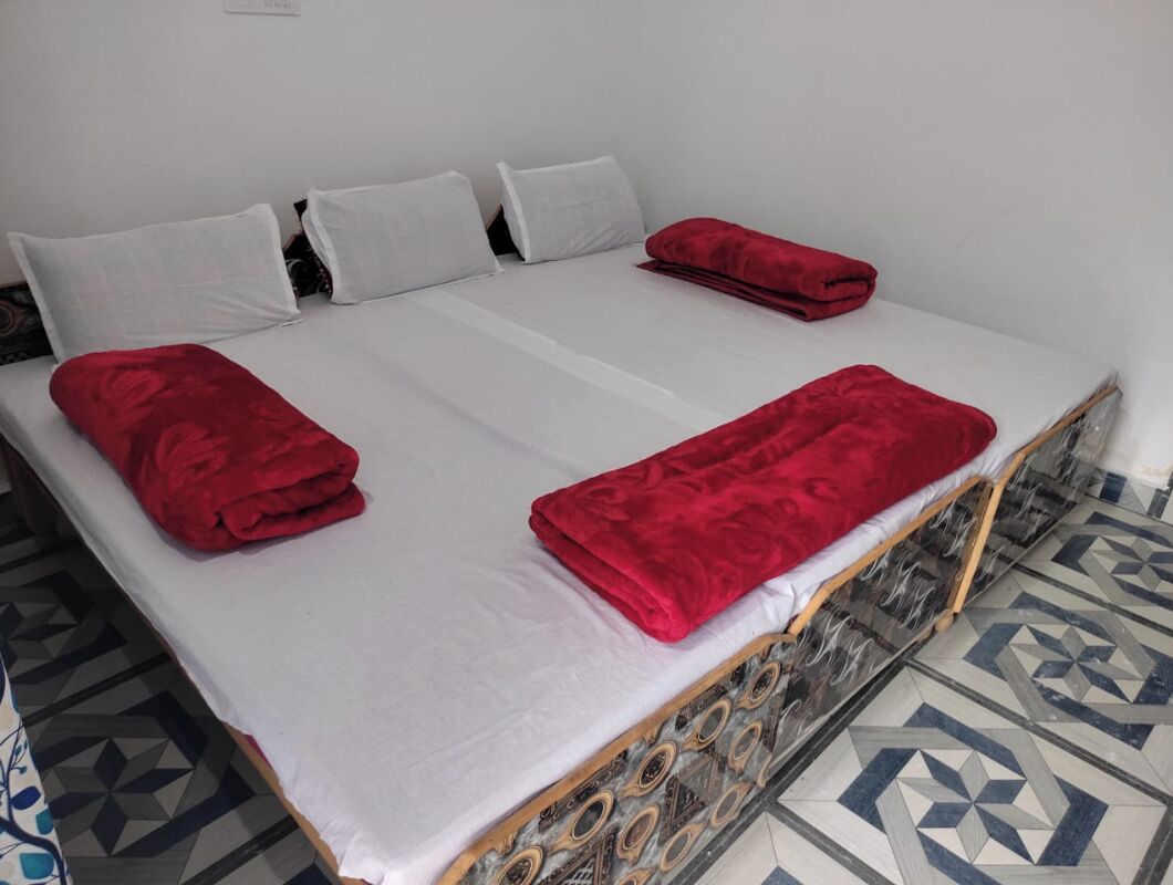 Una cama con sábanas blancas y mantas rojas, un suelo estampado y una pared sencilla.