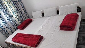 A bed with white sheets, two red blankets, and a patterned bedspread. - Sarvaheet (Ukhimath)