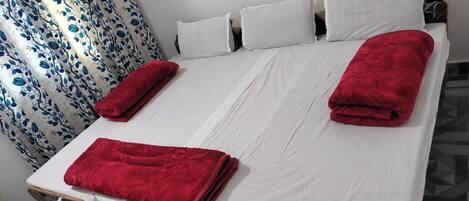 Un lit avec des draps blancs, deux couvertures rouges et une couvre-lit à motifs.