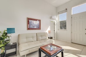 A living room with a sofa, a coffee table, a lamp, a framed picture, and a door with a view. - Near Apollo Beach! Bright Apt w/ Essentials (Ruskin)