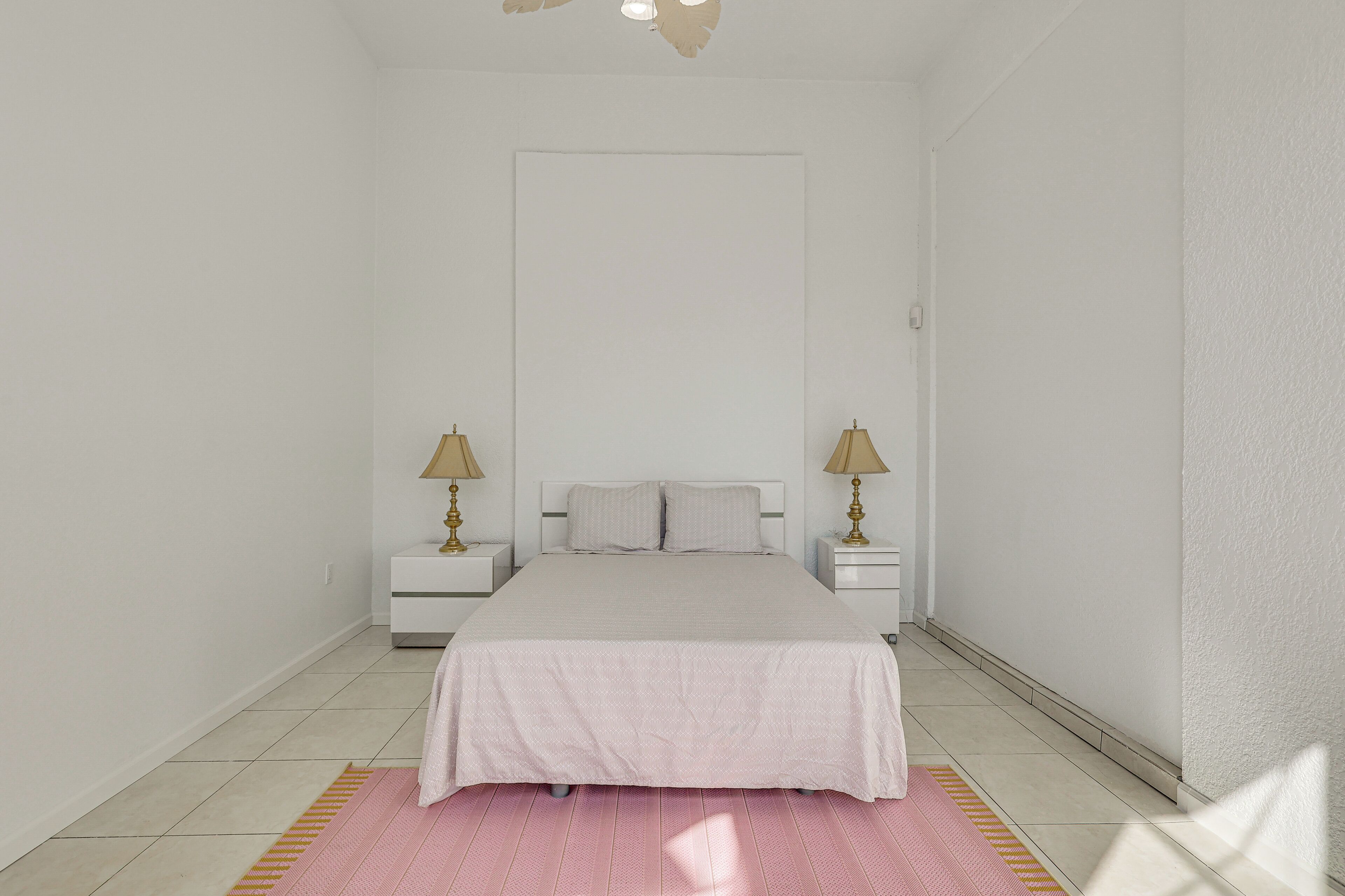 A bedroom with a bed, two bedside tables with lamps, a door, and a pink rug.