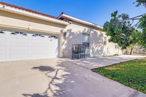 A residential garage with a white door, a small outdoor seating area, and a tree casting shadows on the ground. - Near Apollo Beach! Bright Apt w/ Essentials (Ruskin)