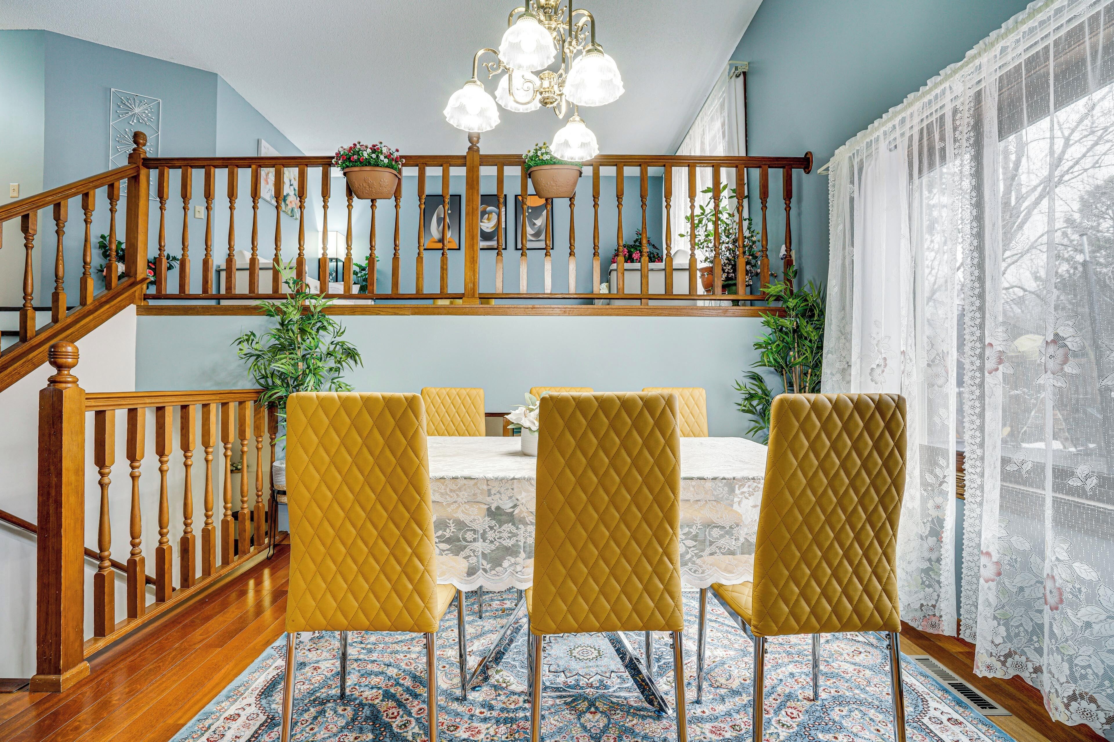 A dining area with a wooden staircase, yellow chairs, and a chandelier.