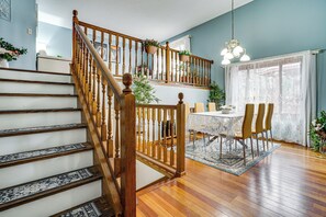 A staircase with wooden railings leading to a second floor, a dining area with a table and chairs, and a chandelier above. - Deck & Outdoor Dining! Spacious St Paul Getaway (Maplewood)