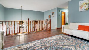 A spacious living room with a wooden staircase, a white sofa with an orange cushion, and a patterned rug. - Deck & Outdoor Dining! Spacious St Paul Getaway (Maplewood)