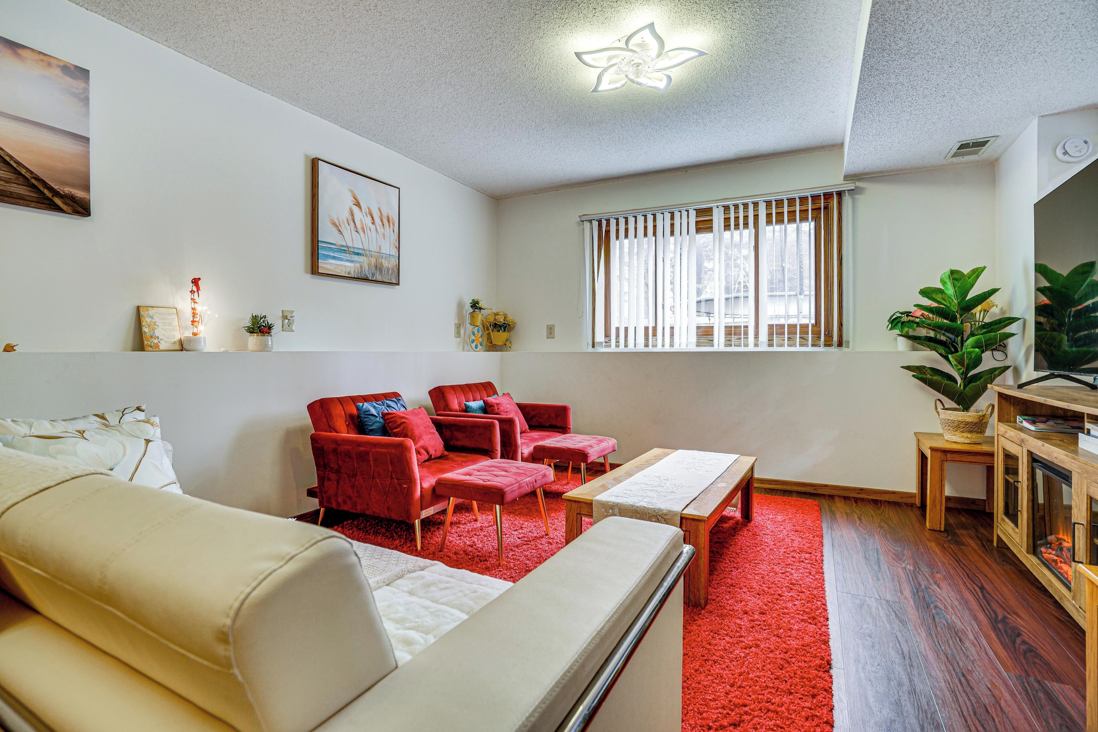 A living room with a red carpet, white sofa, red armchairs, and a wooden cabinet.