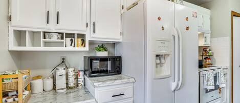 A kitchen with white cabinets, a white refrigerator, a microwave, and a stove.