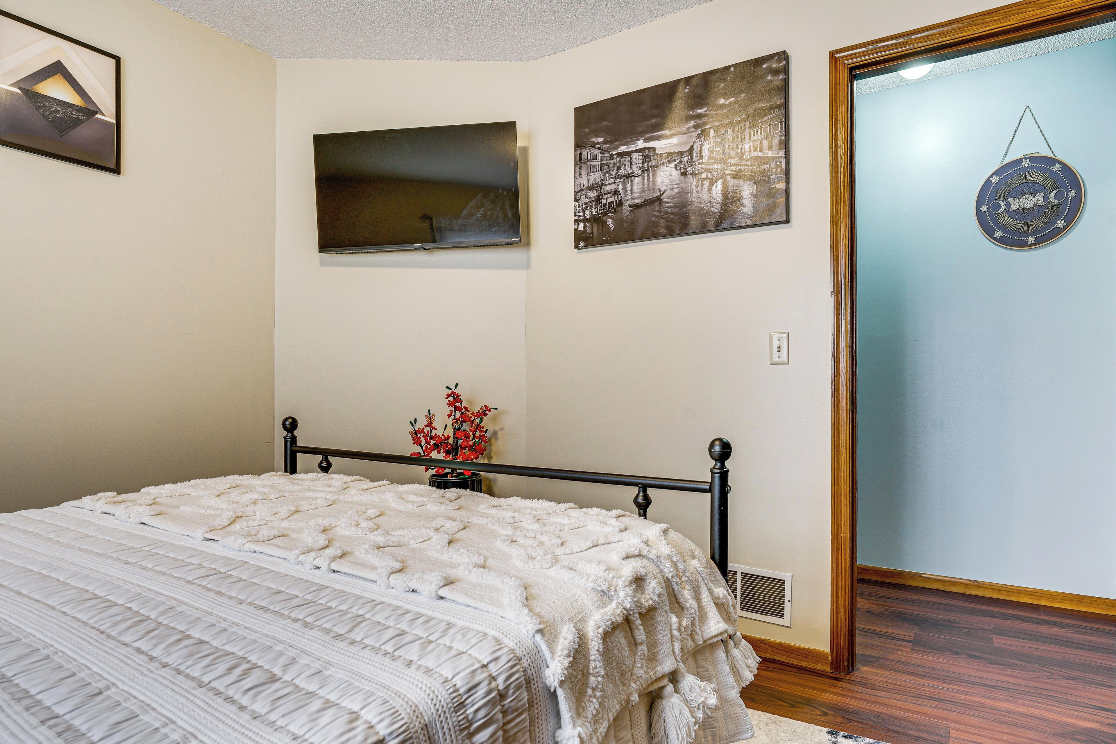A bedroom with a bed, a wall-mounted TV, and artwork.
