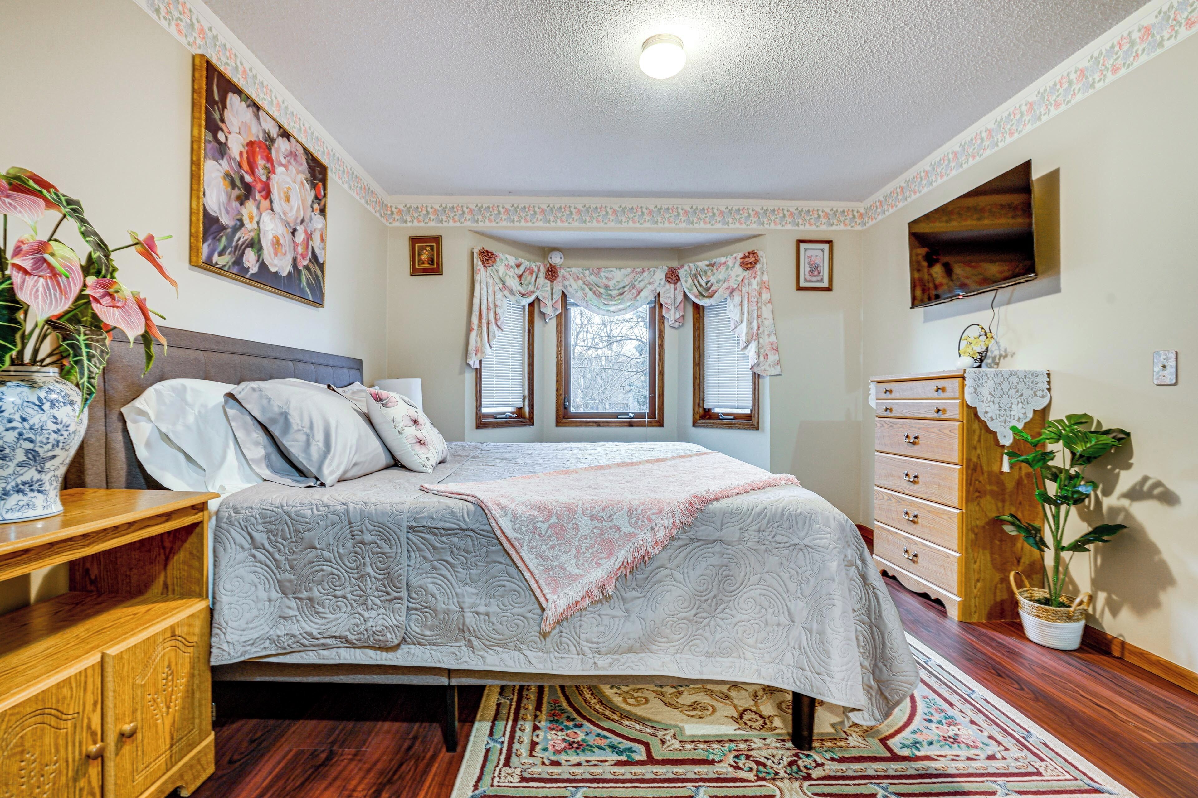Une chambre à coucher avec un lit, une commode et une grande fenêtre avec des rideaux.
