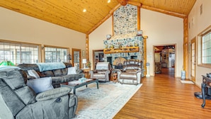 A spacious living room with a stone fireplace, leather sofas, and a wooden ceiling.