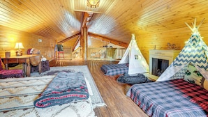 A cozy log cabin interior with a loft bedroom, a fireplace, and a teepee.