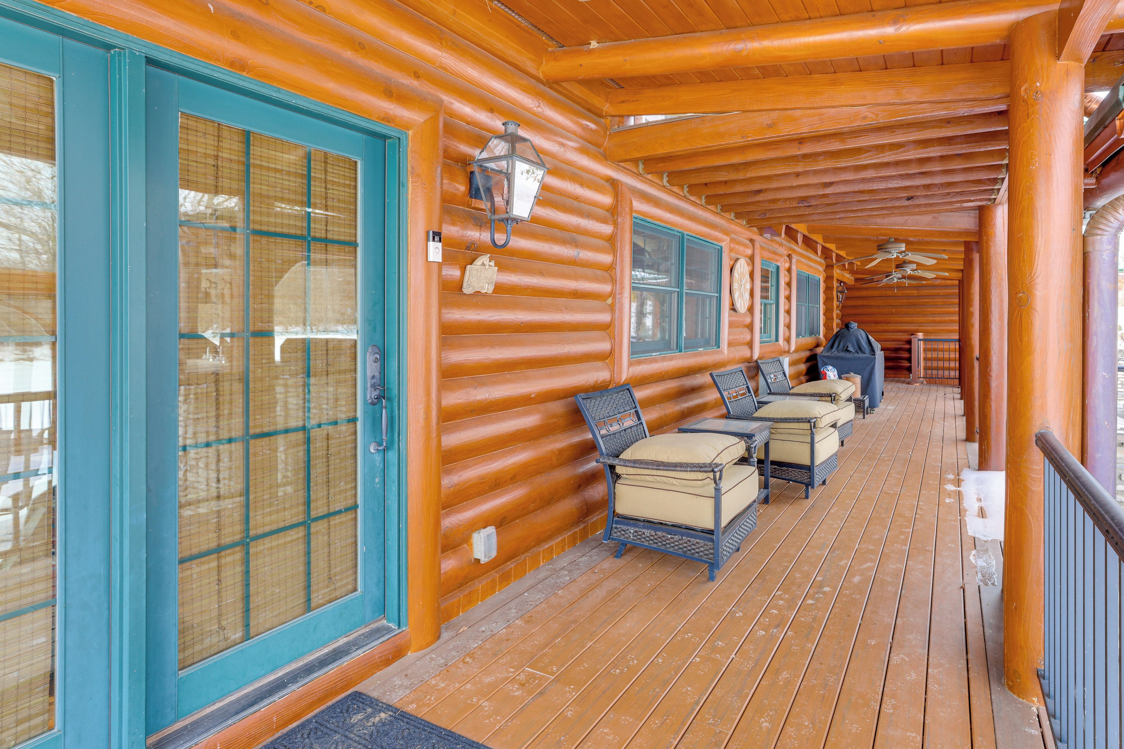 A wooden log cabin with a covered porch, featuring a seating area with chairs and a table.