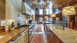 A spacious kitchen with wooden cabinets, a large island, and a red patterned rug. - Theater, Gym, Hot Tub: Versailles 'heritage Lodge' (Versailles)