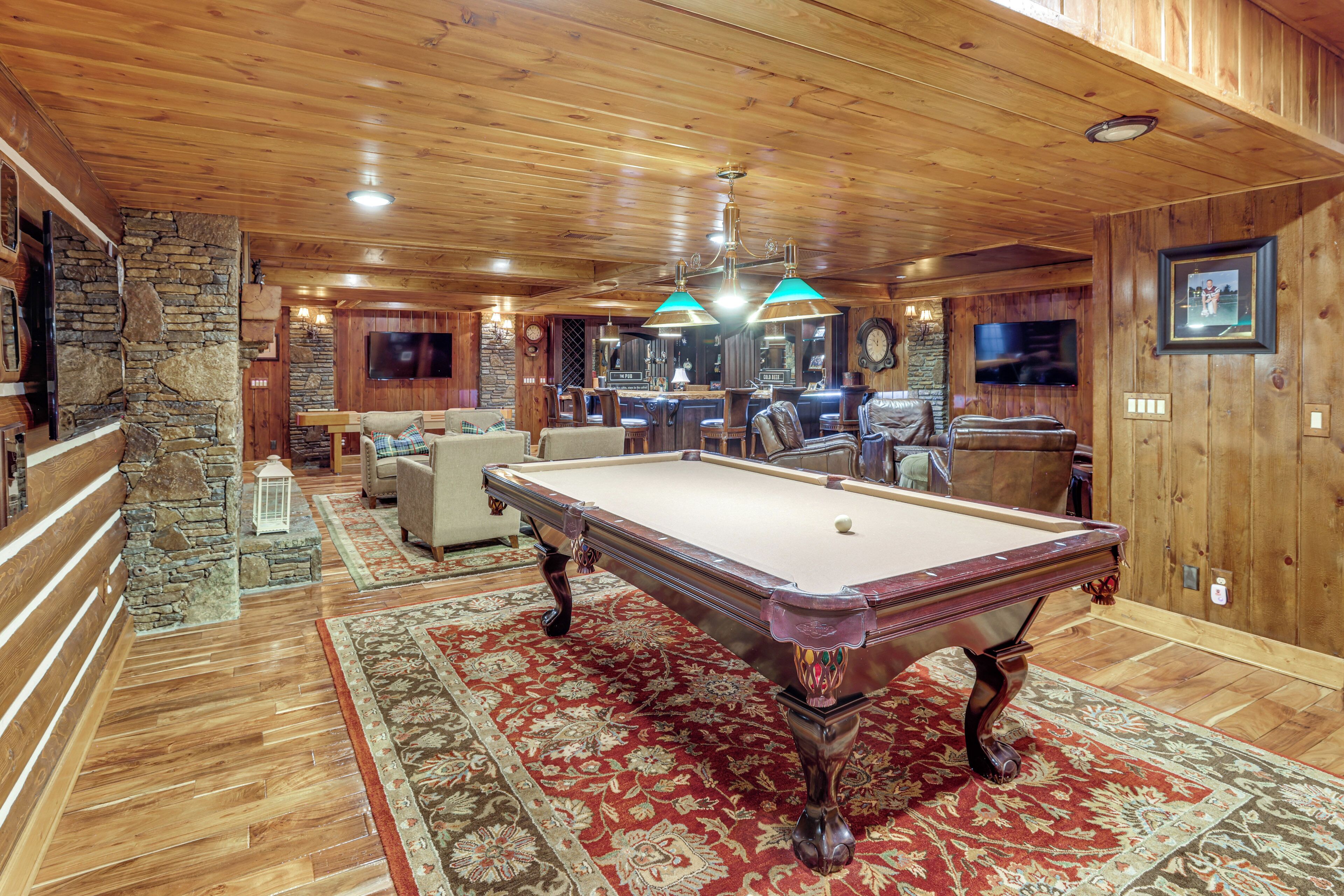 A wooden interior with a pool table, seating area, and stone wall.