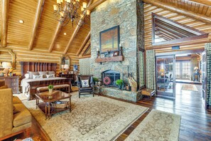 A spacious living room with a stone fireplace, wooden ceiling beams, and a large window. - Theater, Gym, Hot Tub: Versailles 'heritage Lodge' (Versailles)
