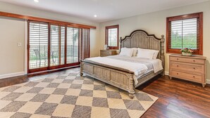 A bedroom with a large bed, wooden headboard, a nightstand, a dresser, and a checkered rug. - Game Room, Hot Tub & Views! Luxe Temecula Estate (Temecula)