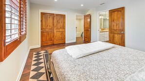 A bedroom with a large bed, wooden wardrobe, and a bathroom visible through an open door. - Game Room, Hot Tub & Views! Luxe Temecula Estate (Temecula)