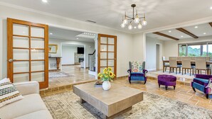 A spacious living room with a beige sofa, a coffee table with a vase of sunflowers, and purple upholstered chairs. - Game Room, Hot Tub & Views! Luxe Temecula Estate (Temecula)