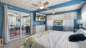 Una camera da letto con un letto, una ventola a soffitto, una cassettiera, una finestra con tende e vista sull'esterno.