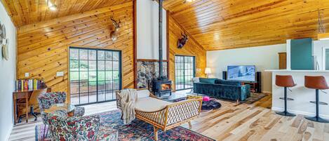 Interior acogedor de una cabaña con techo de madera, chimenea, sofá, una mesa de centro y televisor.