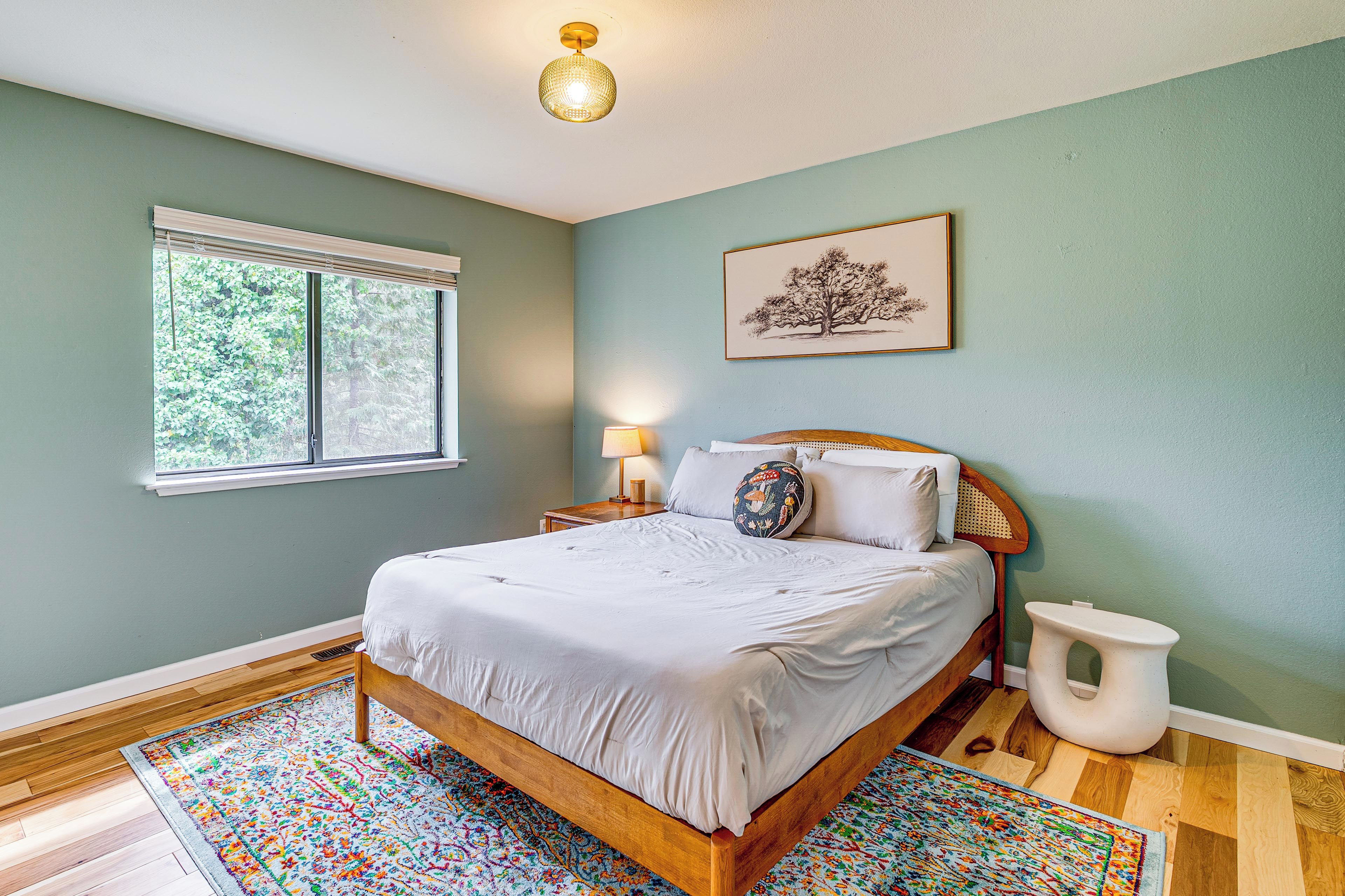 A bedroom with a wooden bed, a window, a bedside table with a lamp, and a wall-mounted picture.
